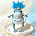 Blue Feather Royal Toad – Hand-Knitted Figurine with Blue Feather Crown, Gold Tiara, Layered Crystal Chains, Pearl Bracelet &amp; Diamond Accents | The Third Space